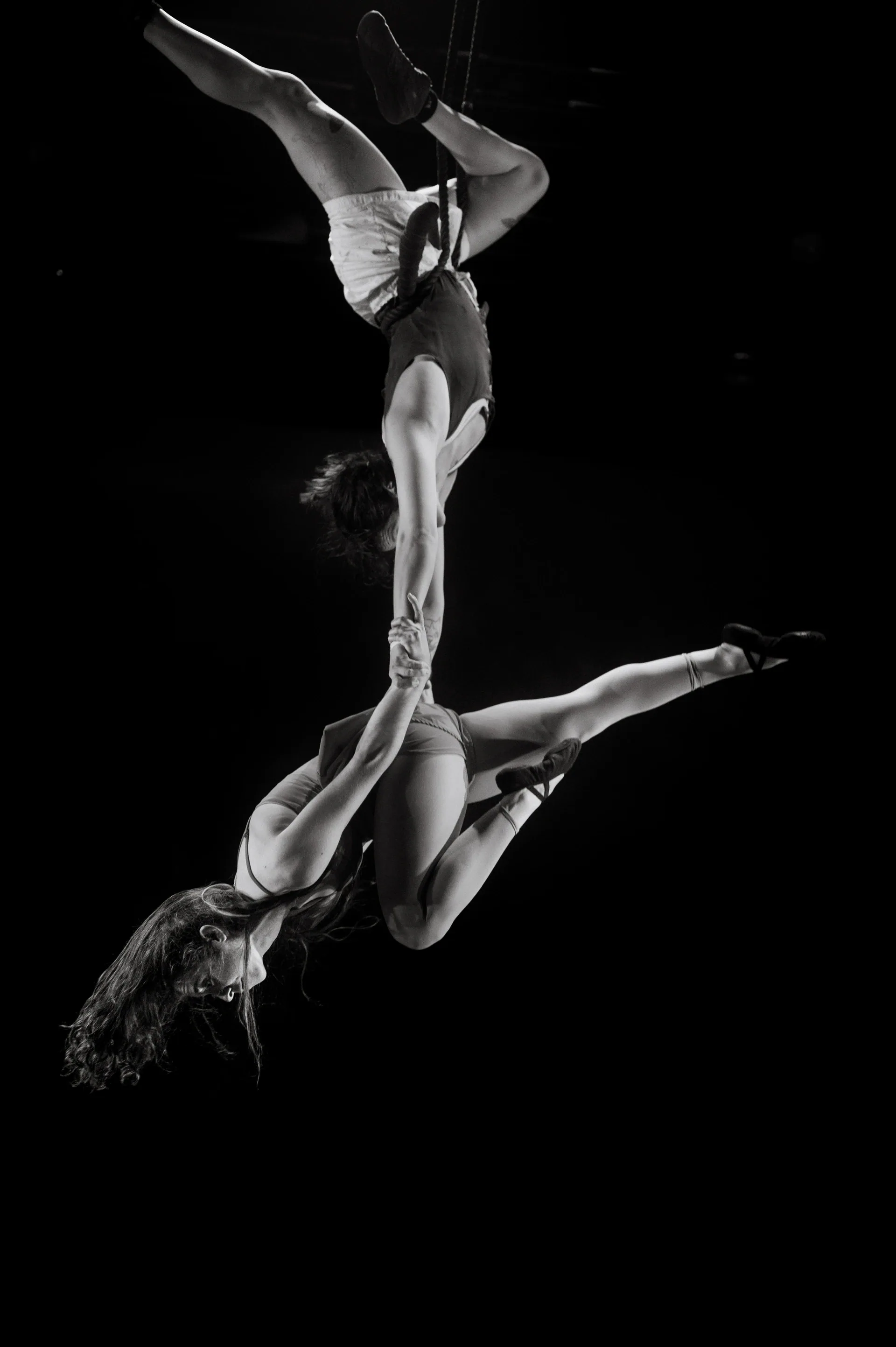 Three acrobats form a vertical suspended chain of bodies.