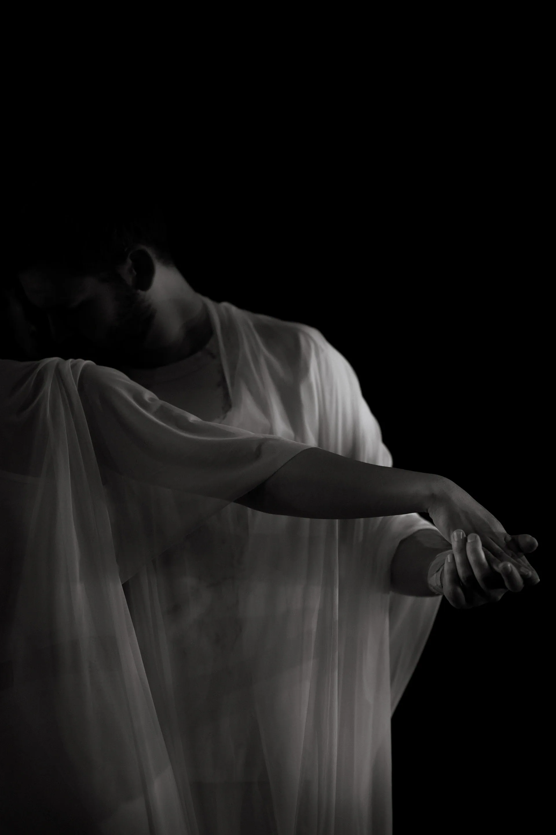 Performer draped in translucent fabric extends both arms.