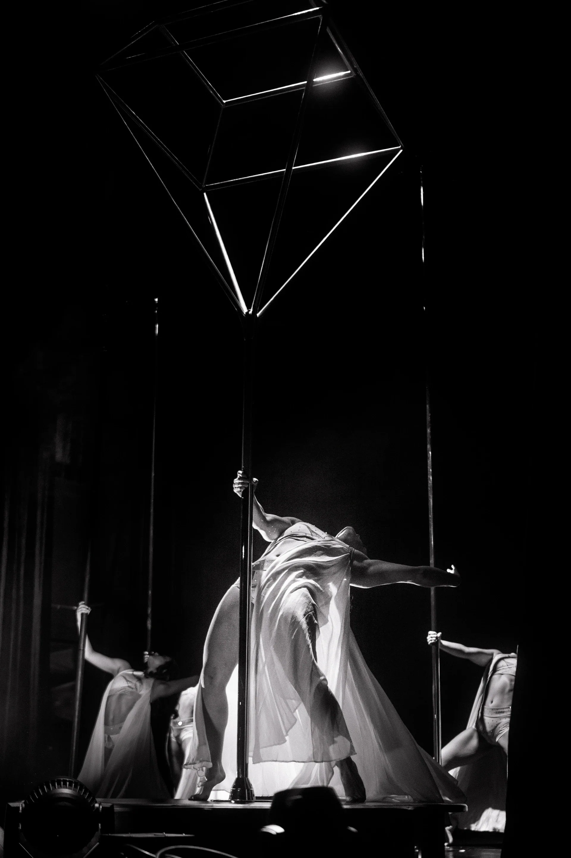 Large angular metal frame hangs above a performer surrounded by draped fabric.