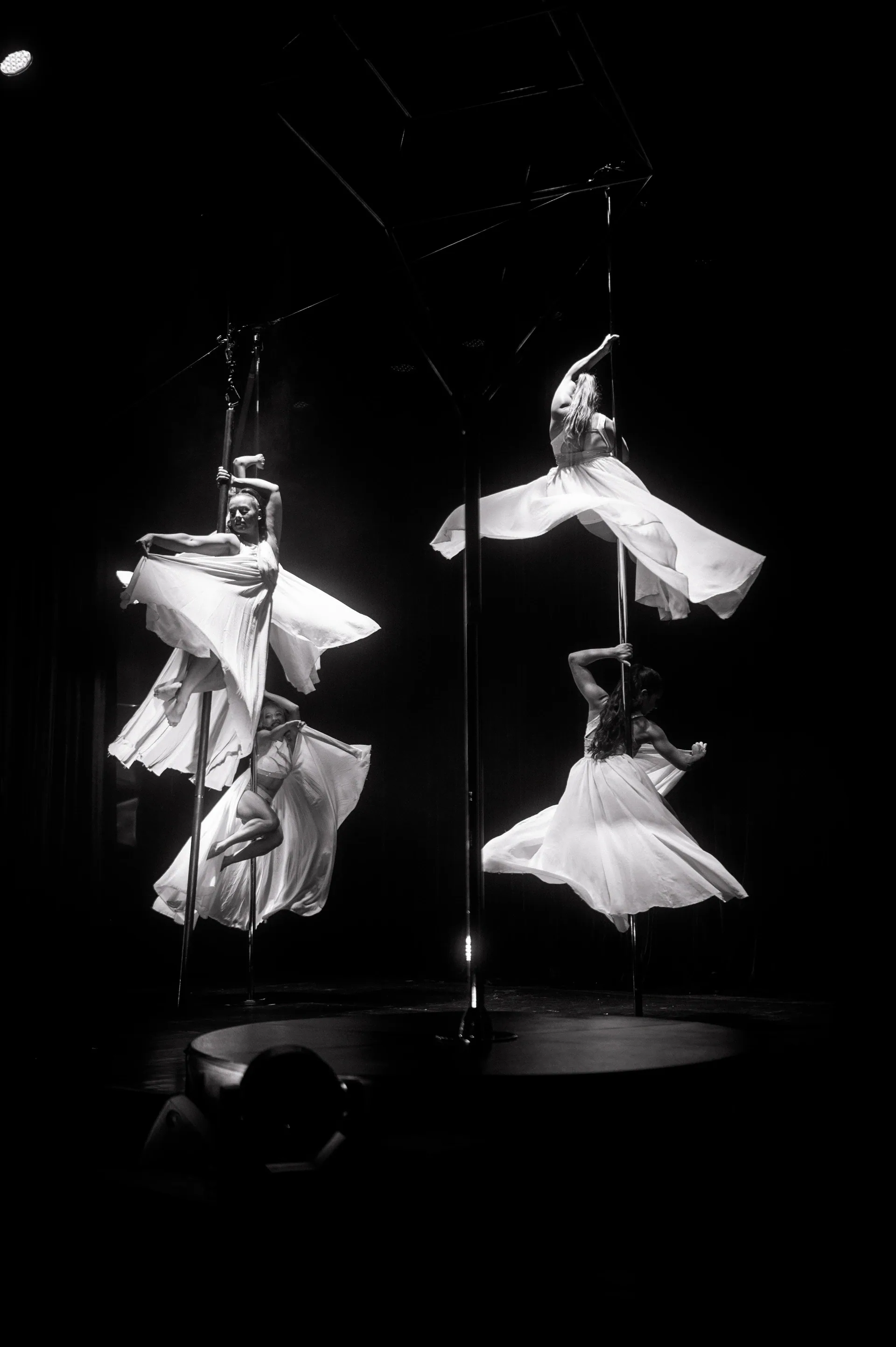 Two aerialists in flowing skirts hold poses on vertical poles.