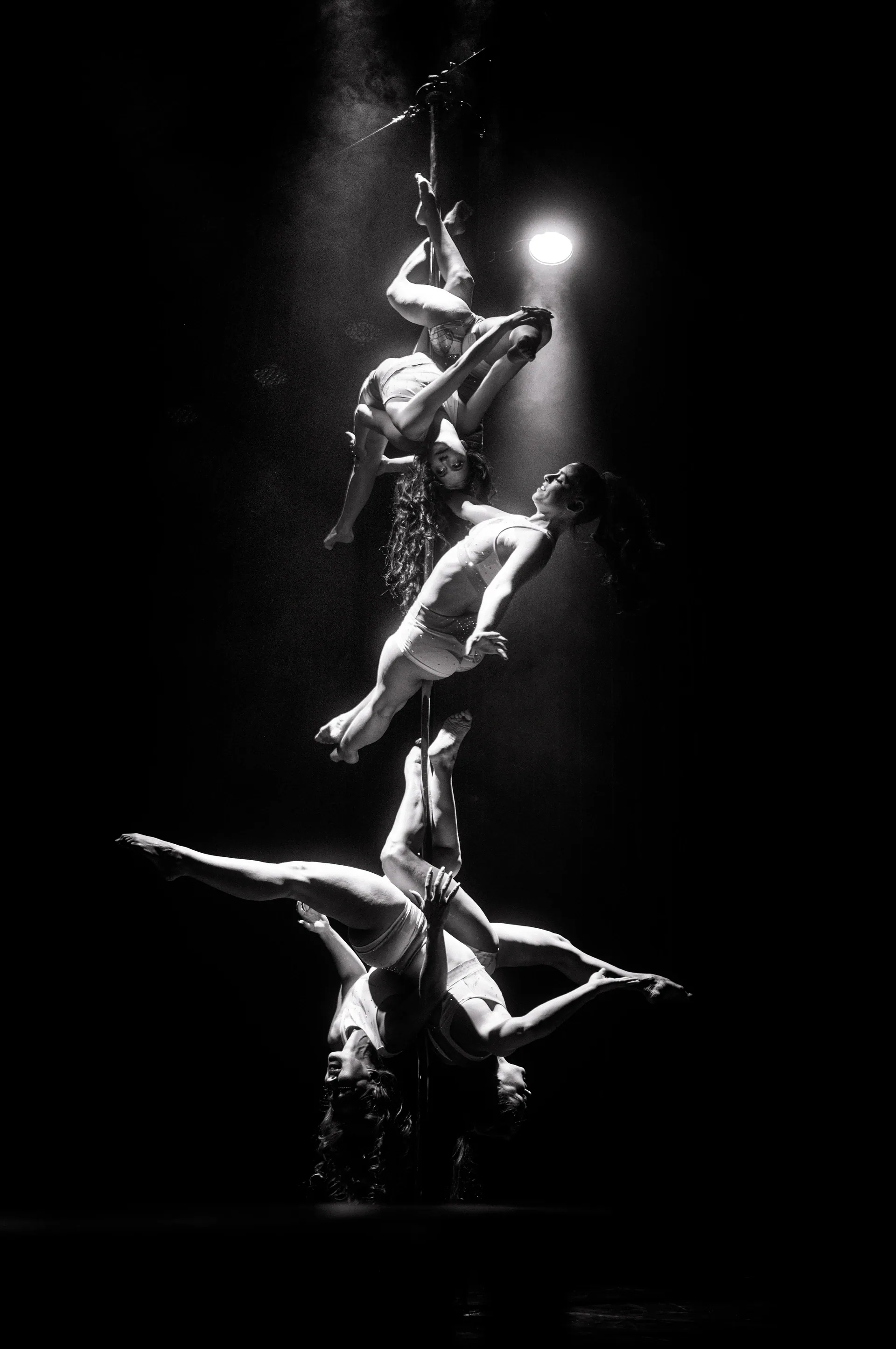 Several acrobats form a vertical stack on a suspended apparatus.
