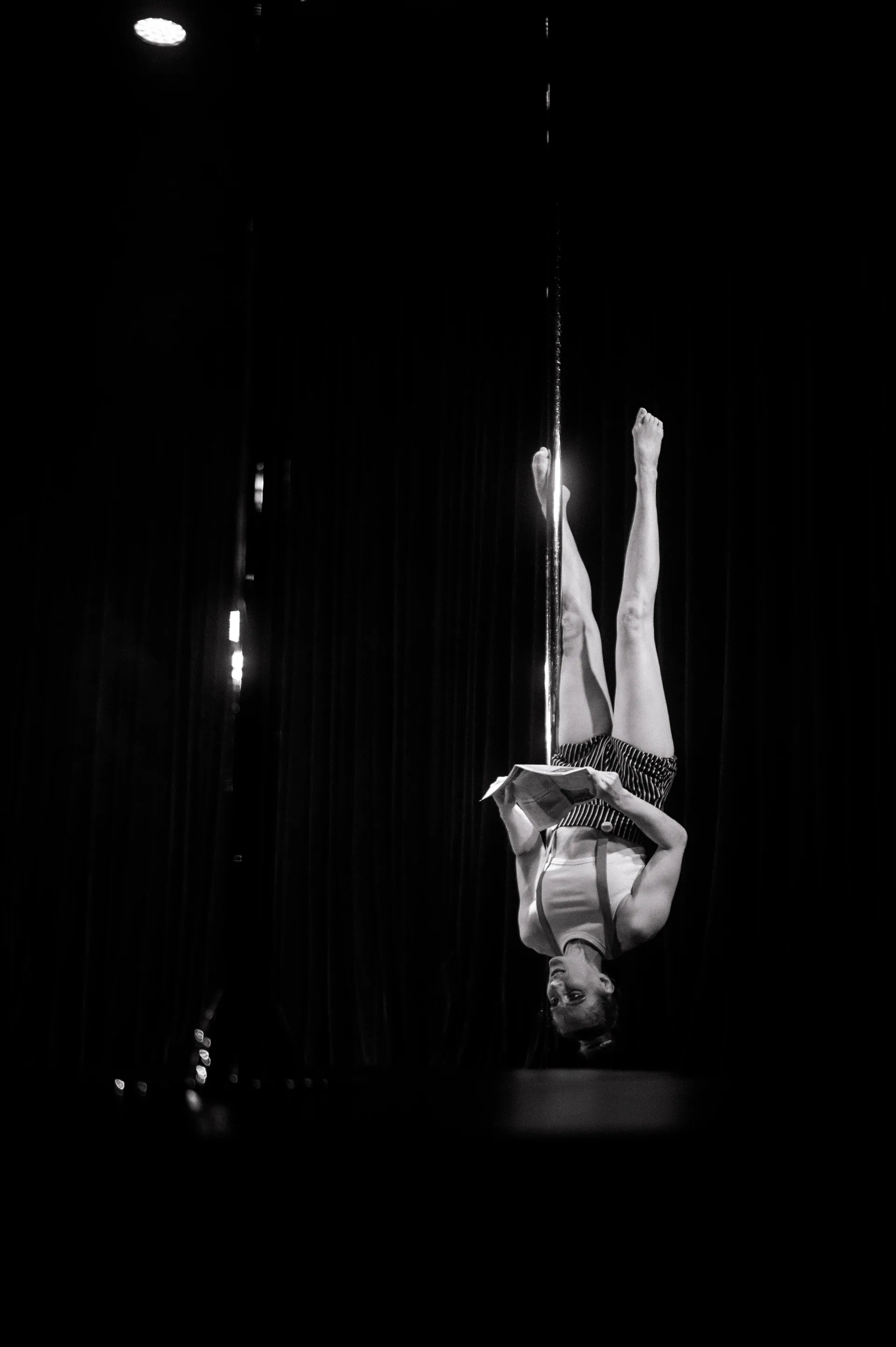 Aerialist hangs upside down from a vertical pole.