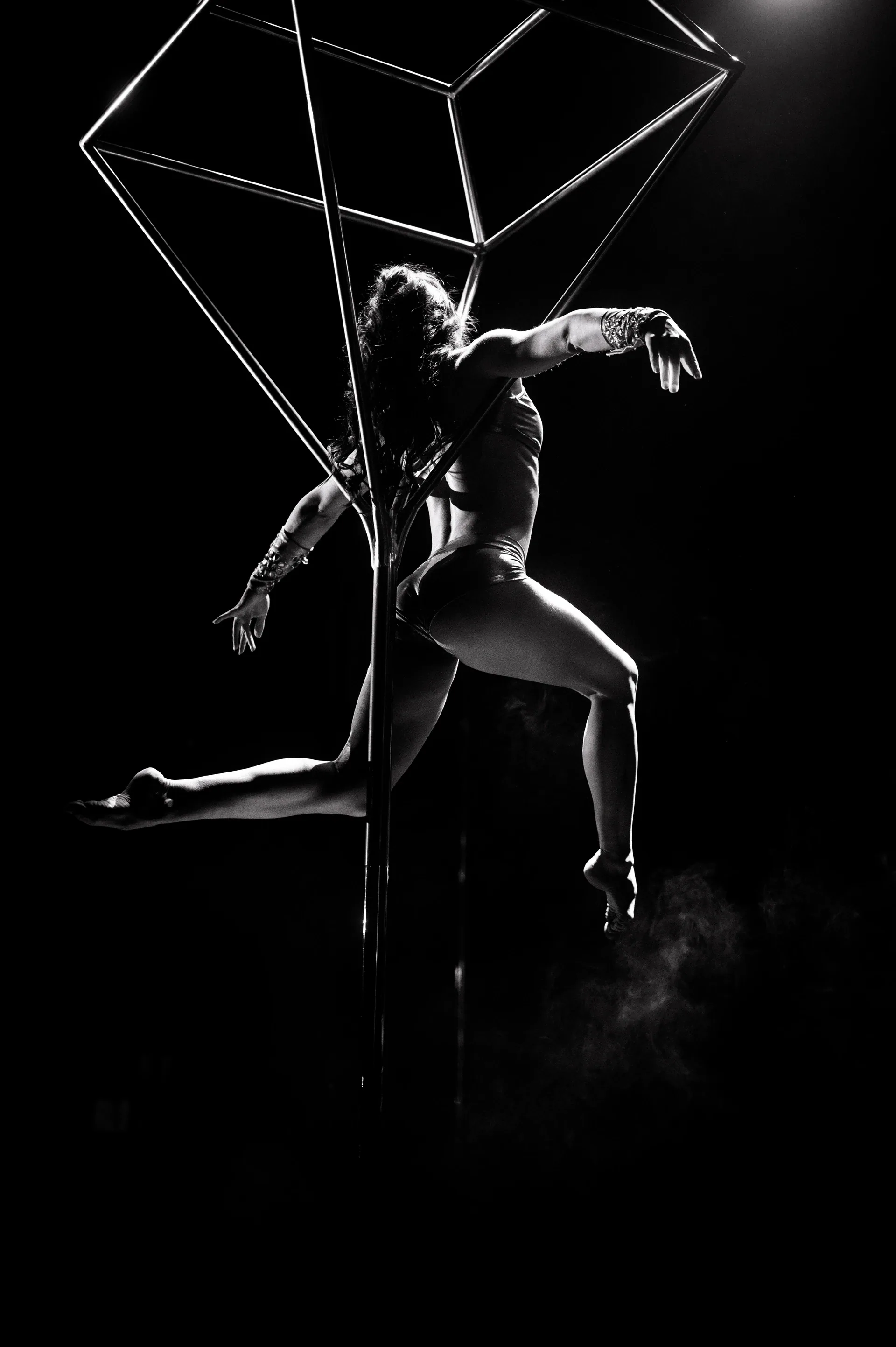 Performer poses inside a tilted geometric metal frame.