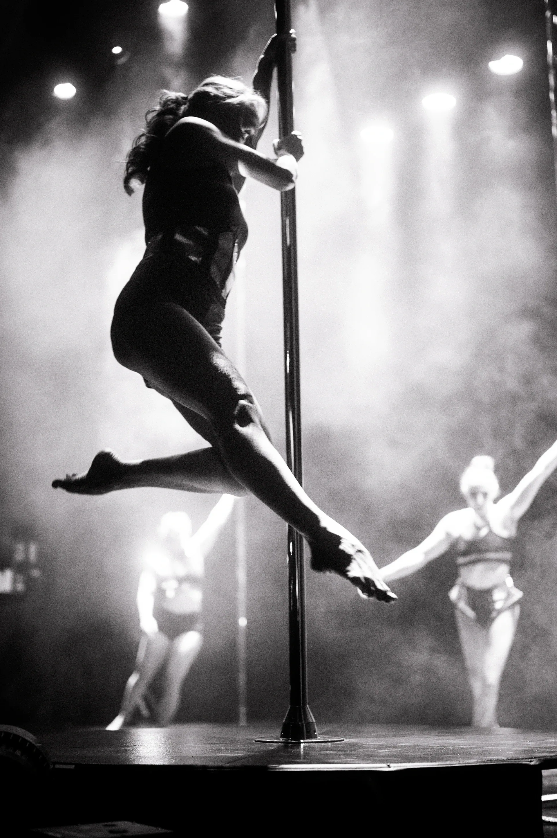 Pole performer extends one leg while climbing above the stage.