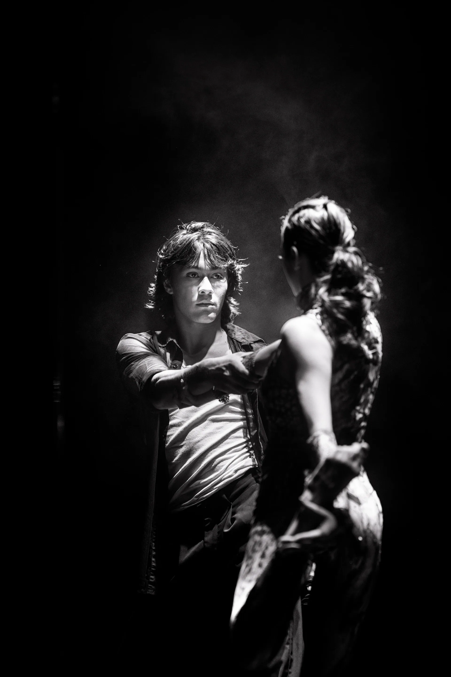 Two performers face each other while one reaches toward the other.