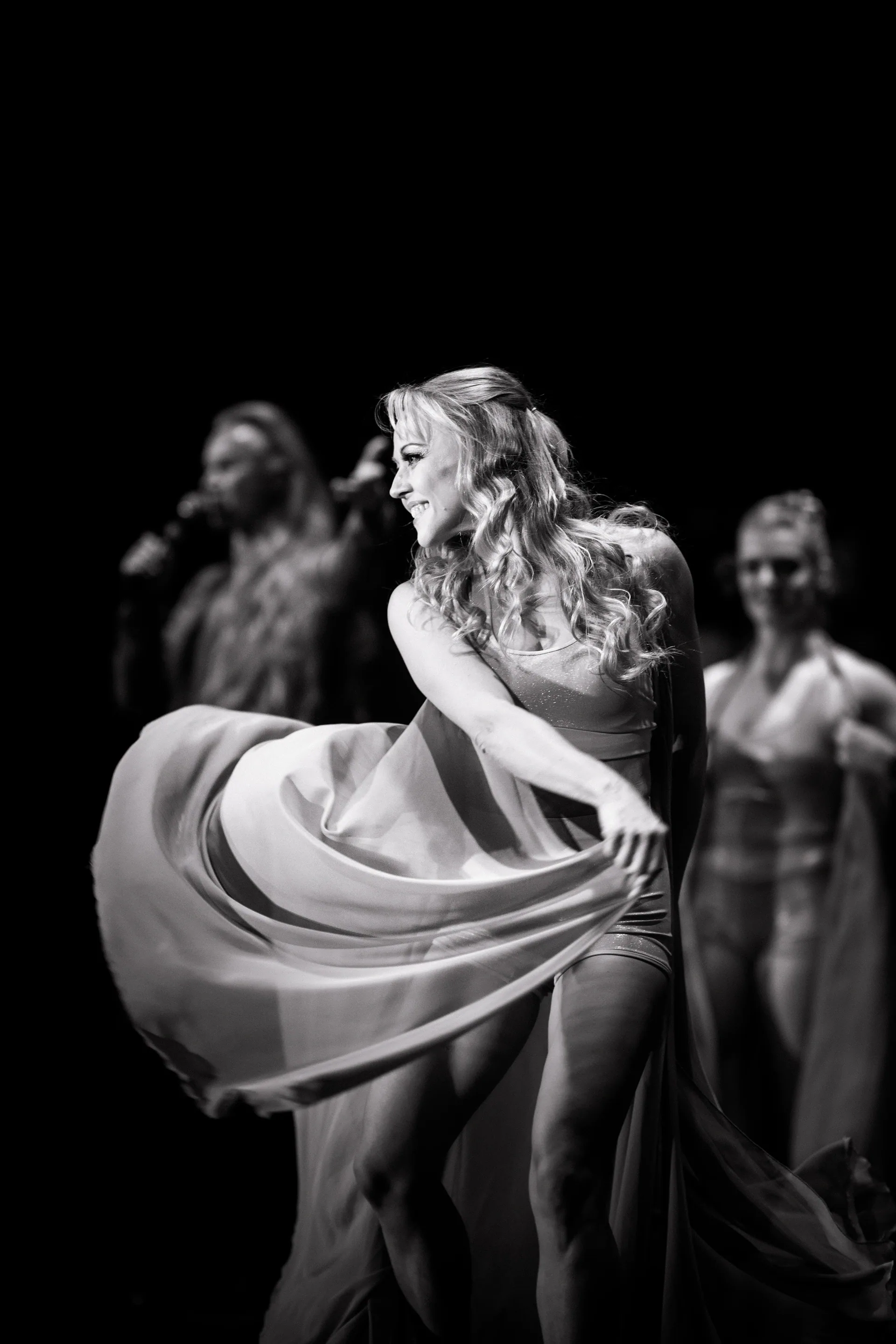 Performer spreads a billowing skirt while others stand behind.
